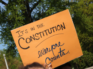 Orange sign that says "It's in the Constitution: Everyone Counts"