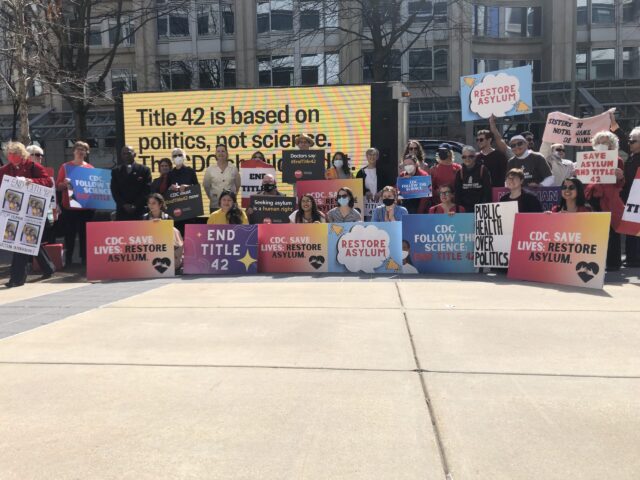 Activists hold signs in front of the CDC Building to End Title 42