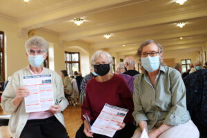 Three older white ladies with gray hair wearing masks look at the camera